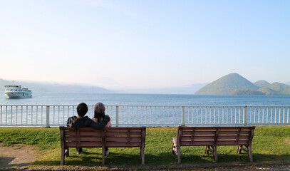 The morning scenery of the sea, sky, mountains, trees, boats and a young couple at Lake Toya in Hokkaido, Japan gives a feeling of freshness and relaxation.