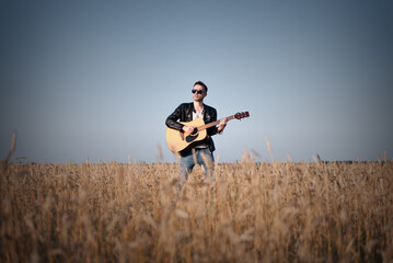 Musician is playing on the guitar among the wheat field.