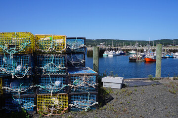 Fototapeta na wymiar Stacked lobster traps on the pier with fishing boats moored in the background at North Head on Grand Manan Island, New Brunswick