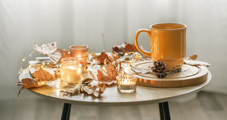 Cozy composition with a cup, candles and autumn leaves in the interior.