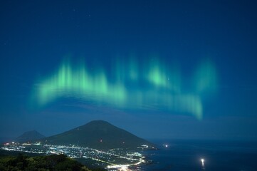 Naklejka na ściany i meble The Northern lights with mountain and city lights in the night at Norway