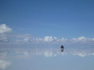 ボリビアのウユニ塩湖にて水面に鏡のように反射する景色の中をドライブする車