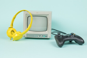 Retro monitor, yellow headphones and a game console on a blue background.