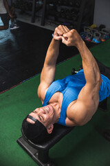 A fit man does a lying isometric chest squeeze on a bench while at the gym. Contracting and flexing...