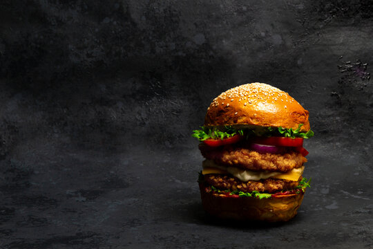 Fresh tasty breaded chicken burger on dark background. Big cheeseburger with double cutlet. Fat unhealthy street food.