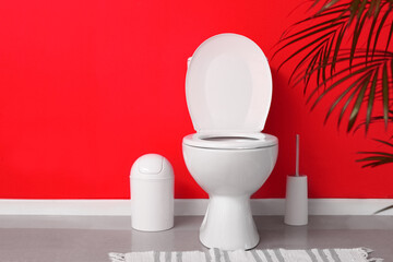 Modern toilet bowl in interior of restroom near red wall
