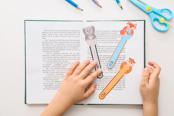 Little child with cute bookmarks reading book on white background
