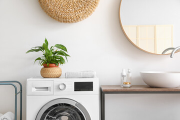 Modern washing machine with houseplant and towel in bathroom