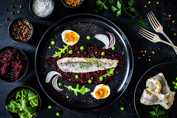 Marinated herring fillet with beetroots puree, hard boiled boiled egg, onion and green peas on wooden black table
