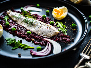 Marinated herring fillet with beetroots puree, hard boiled boiled egg, onion and green peas on...