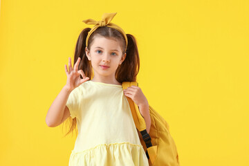 Cute little school girl showing OK gesture on color background