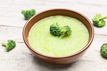 Bowl of tasty broccoli cream soup on light wooden background