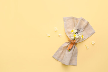 Fototapeta na wymiar Stylish cutlery with napkin and narcissus flowers on color background