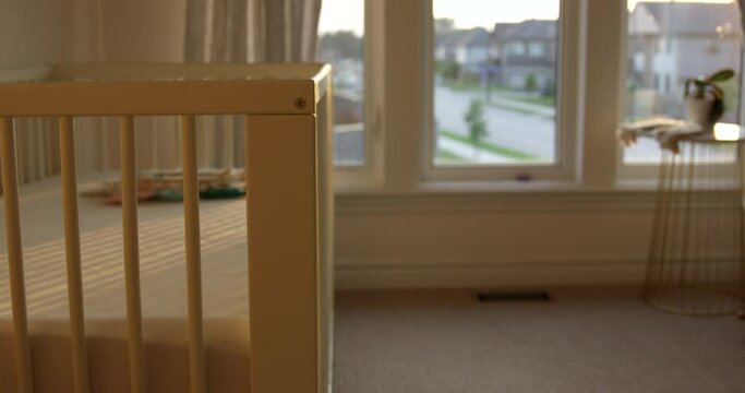 Empty baby crib in baby room as sun sets outside - hand held