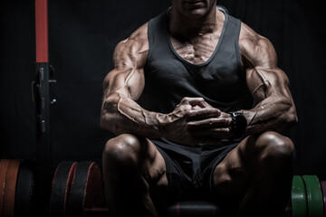 Very muscular bodybuilder man with veins on the body sitting in dim light. Gym training. Fit and...