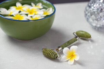 Beautiful spa composition with plumeria flowers. Face roller and guasha massager. Facial skin care, anti age products and creme. Chinese Gua Sha massage tools.