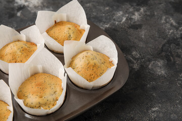 Baking tin with delicious poppy seed muffins on dark background