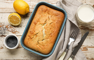 Baking tin with delicious poppy seed cake and cutlery on wooden background