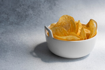 Crispy salty potato chips or crisps in bowl on white background. Unhealthy food concept.