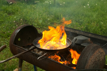 Man is frying slices of fresh organic zucchini on frying pan with hot boiling oil on coals in grill. He is putting zucchini in hot oil and its starting to burn. Preparing food in chargrill on nature.