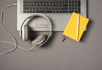 Top view photo of laptop keyboard wired white headset pen and yellow notepad on isolated grey background