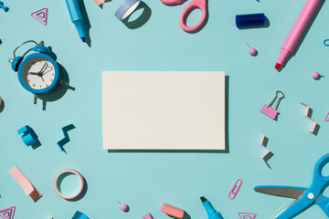 Top view photo of white card bicolor blue and pink school accessories stationery markers binder clips pins eraser adhesive tapes scissors and alarm clock isolated light blue background with copyspace