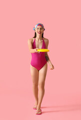 Beautiful young woman in swimsuit playing frisbee on color background