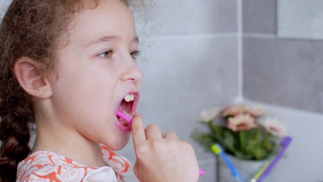 Portrait happy cute young teenage girl brushing teethin the morning in bathroom and smiling. Children daily healthcare routine. Caucasian kid with white tooth looking at mirror isolated at home.
