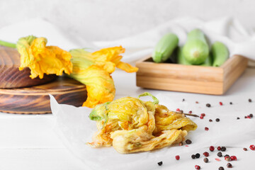 Parchment with fried zucchini flowers and spices on light wooden table, closeup