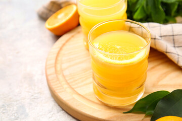 Board with glass of tasty orange juice on light background, closeup