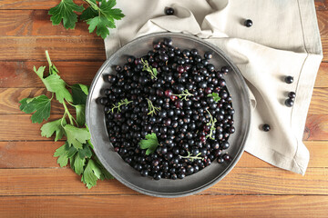 Plate with ripe black currant on wooden background