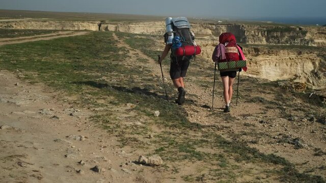 backpacking in mountains, two hikers are walking with backpacks and sticks