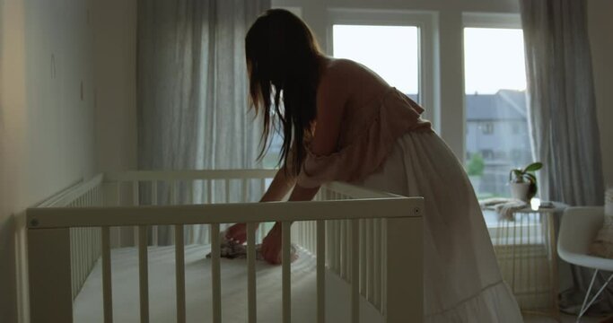 Expecting mother pregnant places small toy on babys crib