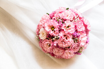 A bouquet of pink flowers on the skirt of a white wedding dress