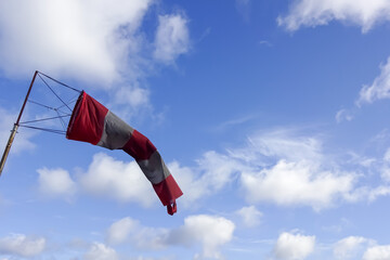 Close up of red and white windsock indicator on blue sky with many white clouds background.