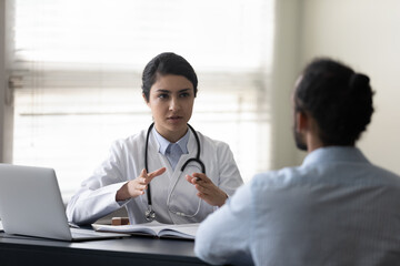 Concentrated young female indian doctor physician giving healthcare consultation to african...