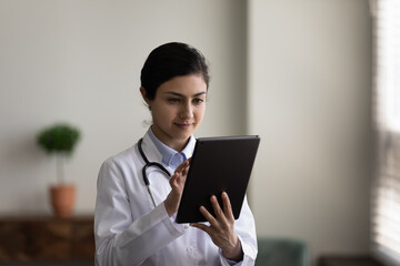 Concentrated young indian female doctor general practitioner therapist using applications on...