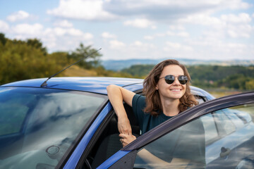 Young happy female driver resting near her car enjoying view of summer nature. Travel destinations