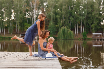 mom and daughters walk by the water on a wooden bridge