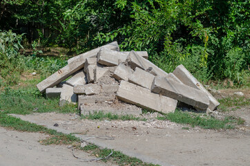 A pile of old concrete curbs piled on the side of the road. Gree