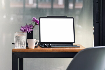Mockup blank screen tablet with magic keyboard on wooden tabler in modern office room.