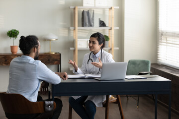 Confident skilled young indian female general practitioner doctor in medical uniform giving...