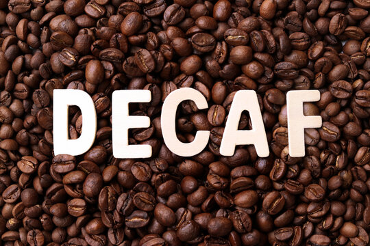 Decaf coffee word on roasted coffee beans background. Concept of decaffeinated coffee or low caffeine coffee.