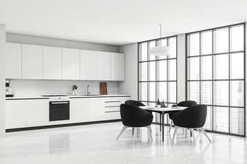 White kitchen space with panoramic windows and black armchairs. Corner view.