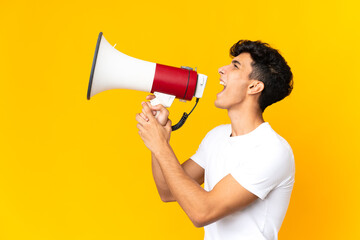 Young Argentinian man isolated on yellow background shouting through a megaphone to announce something in lateral position