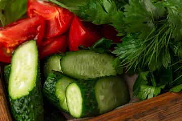 Wooden plate with a lot of herbs and vegetables. Tomatoes cucumbers. parsley and dill. Close-up. Vegetarianism, vitamins and health from nature.