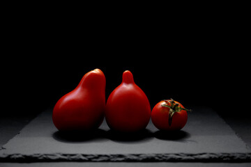 Three red tomatoes on a black background. Tomato isolated, side view. Natural antioxidants in tomatoes