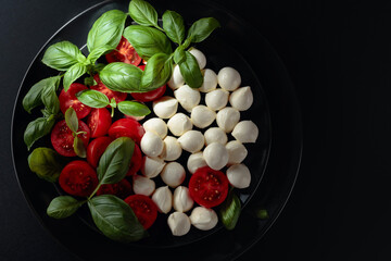 Caprese salad with tomato, mini mozzarella and basil on a black plate.