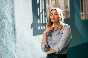 Fototapeta premium Blonde woman wearing denim shirt and black leather skirt standing in the street.