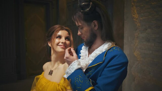 Enchanted fantasy mythical male prince gently inhales scent of hair beautiful fantasy woman. Man king face with beard, ram horns on head blue retro vintage costume. Lady redhead brunette. yellow dress